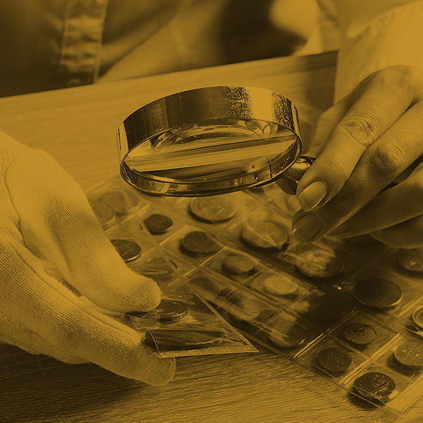 Photo of magnify glass in hand, looking at a coin collection.